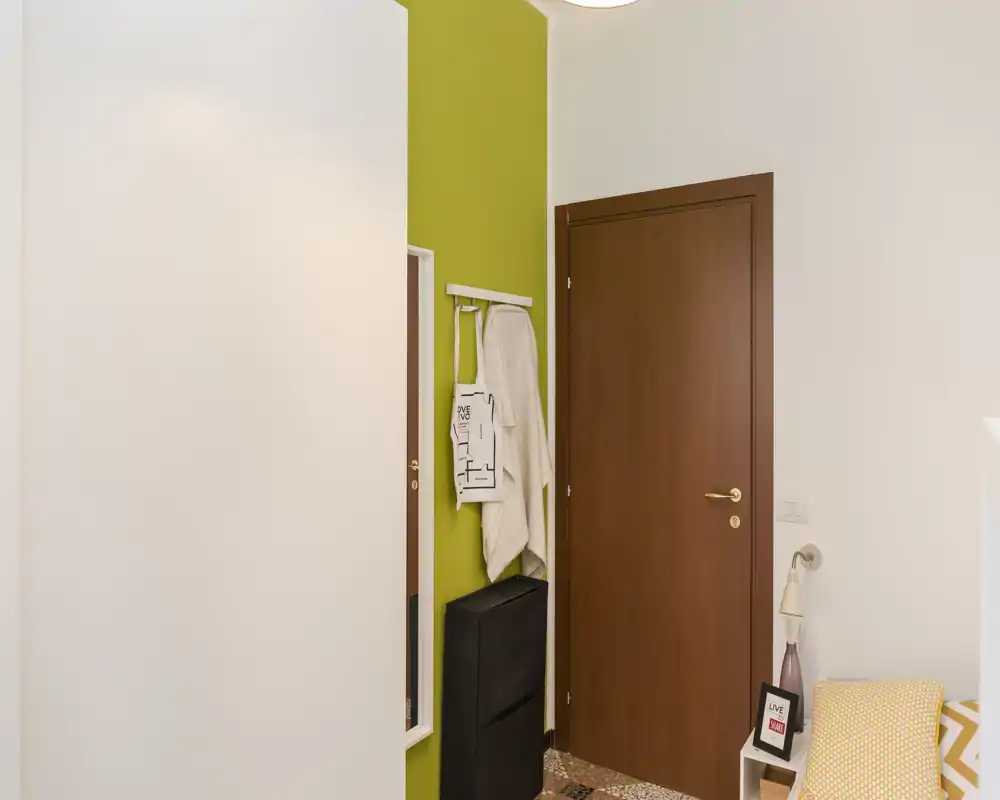 Small, tidy entrance with a wooden door, wall hooks, a mirror strip and a compact storage unit — bright, modern entryway ideal for a flat.