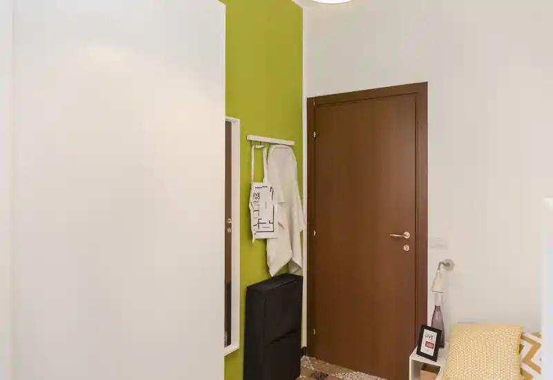 Small, tidy entrance with a wooden door, wall hooks, a mirror strip and a compact storage unit — bright, modern entryway ideal for a flat.