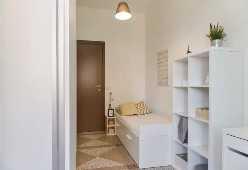 Compact, well-lit bedroom with a single bed, decorative cushions and open shelving — ideal for a cozy single stay.