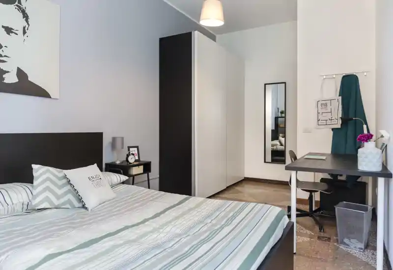 Camera da letto moderna e luminosa con letto ampio, comodino, armadio e una piccola scrivania — linee pulite e tessuti morbidi creano un ambiente accogliente e funzionale.