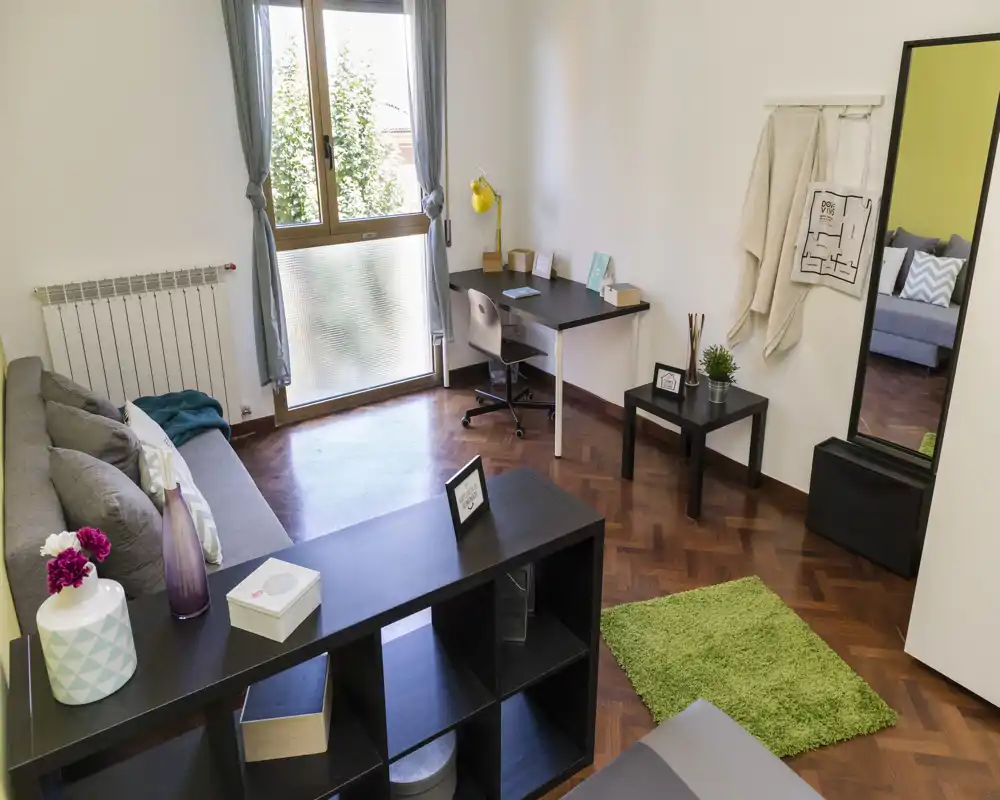 Bright, well-staged living room with a comfortable sofa, workspace by the window and tasteful decorative accents creating a welcoming atmosphere.