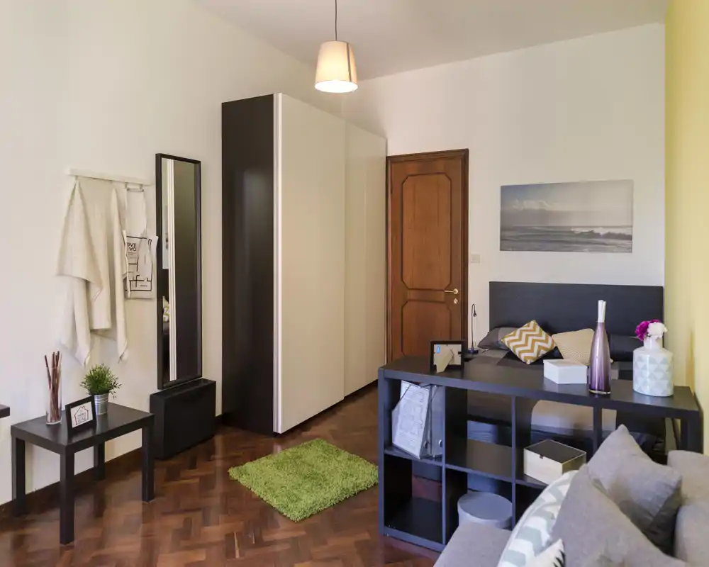 Bright and cozy bedroom with a double bed, headboard and decorative pillows, wardrobe and shelving creating a functional living space.