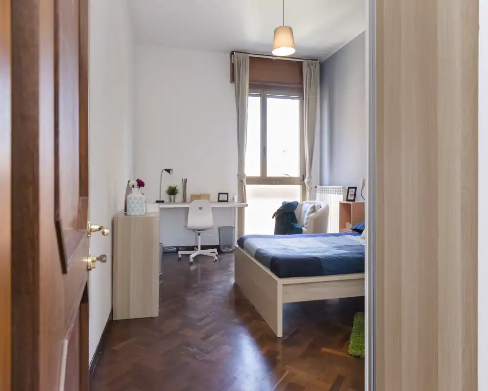 Bright, tidy bedroom with a wooden bed, desk by the window and warm parquet floors — ideal for a comfortable stay.