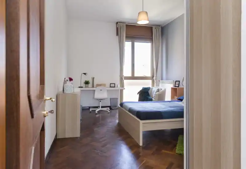 Bright, tidy bedroom with a wooden bed, desk by the window and warm parquet floors — ideal for a comfortable stay.