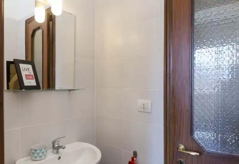 Compact bathroom with a small sink, wall mirror and tiled walls; bright and clean space suitable for a guest WC.