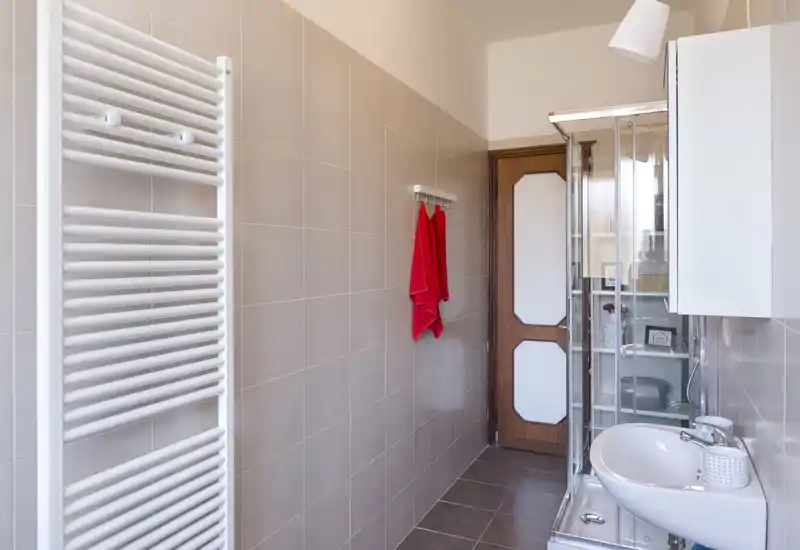 Bagno luminoso e ordinato con lavabo, doccia con box in vetro, scalda-salviette e piastrelle neutre — compatto e ben tenuto.