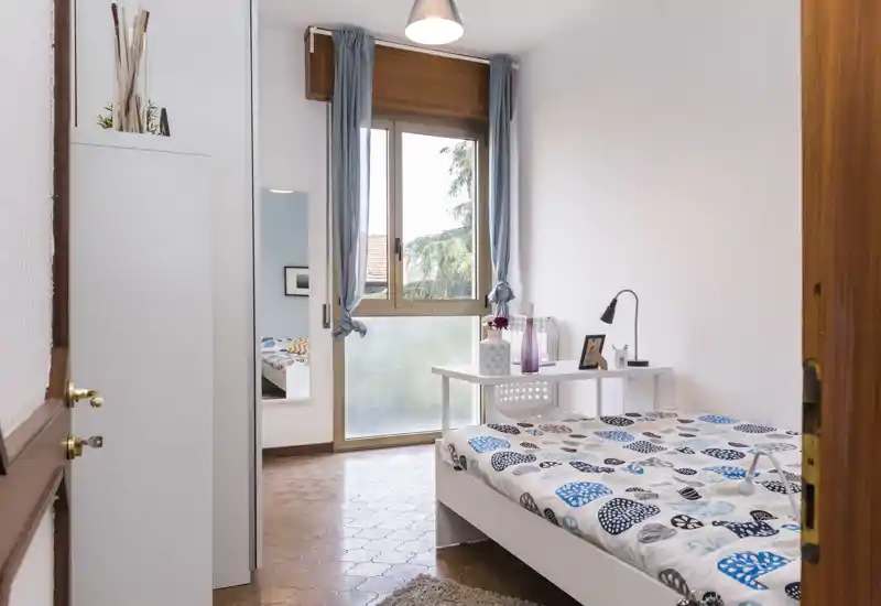 Bright, neatly staged single bedroom with a bed, small desk and large window offering natural light — ideal for a solo renter.