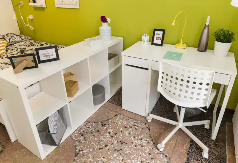 Compact bedroom corner with a white desk, shelving unit and a partially visible bed against a bright green wall; ideal for a single occupant seeking a tidy, modern workspace-bedroom layout.