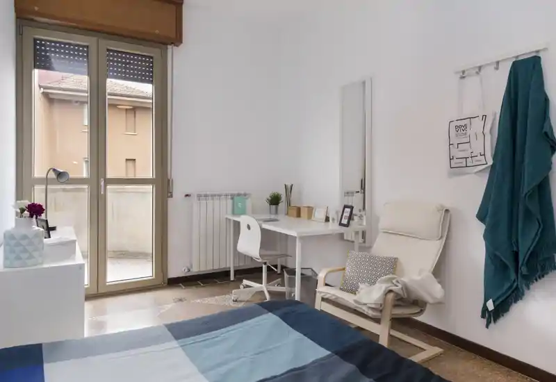 Camera da letto luminosa e ben allestita con letto in primo piano, una postazione di lavoro vicino alla finestra e una poltrona accogliente.