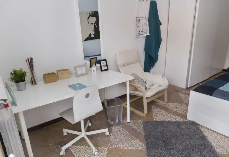 Bright, tidy bedroom corner with a desk, armchair and part of the bed. Ideal for a student or single occupant, the space offers a work area and cozy textiles.