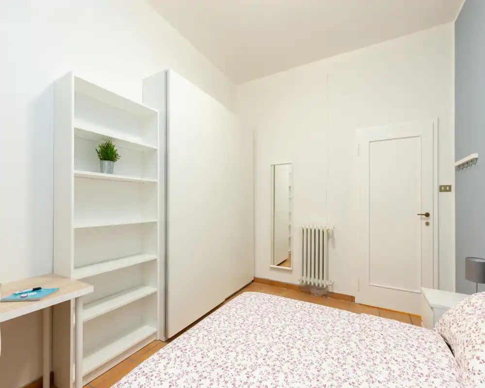 Bright, minimal bedroom with a patterned double bed, white shelving and clean lines — ideal for a calm stay.