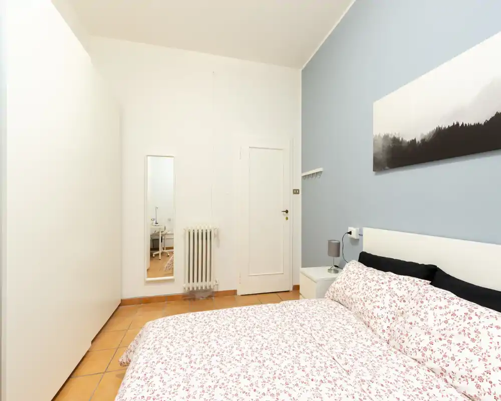 Bright, tidy bedroom with a floral bedspread, bedside table and soft wall art — ideal for a cozy stay.