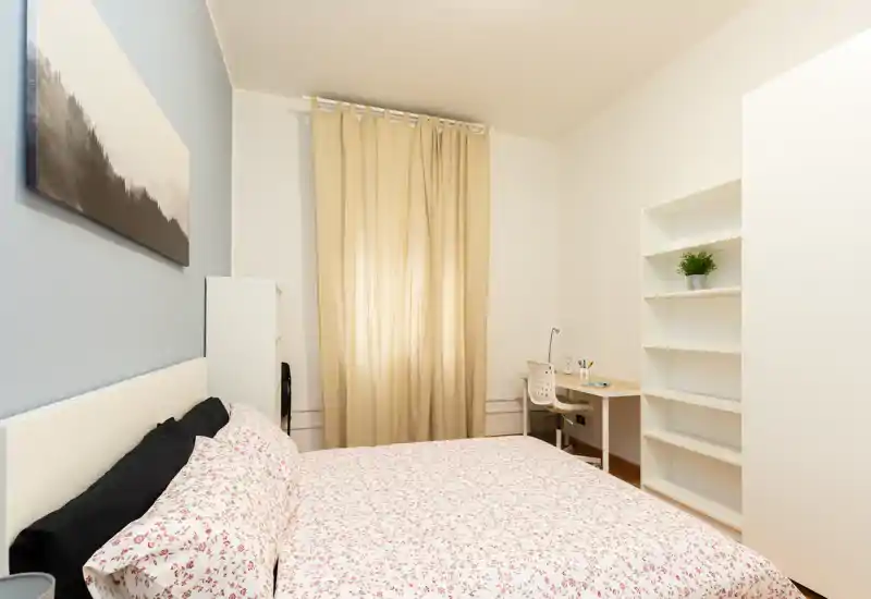 Dormitorio luminoso y acogedor con cama doble con ropa de cama estampada, pequeño escritorio y estantería: ideal para descansar y trabajar ligeramente.