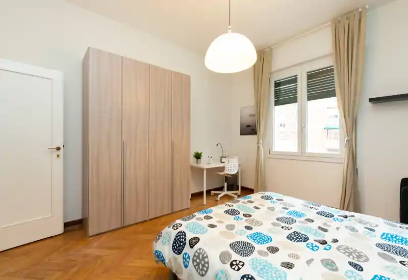 Dormitorio luminoso y ordenado con cama doble en primer plano, amplio armario, pequeño escritorio y ventana que aporta luz natural—ideal para una estancia cómoda.