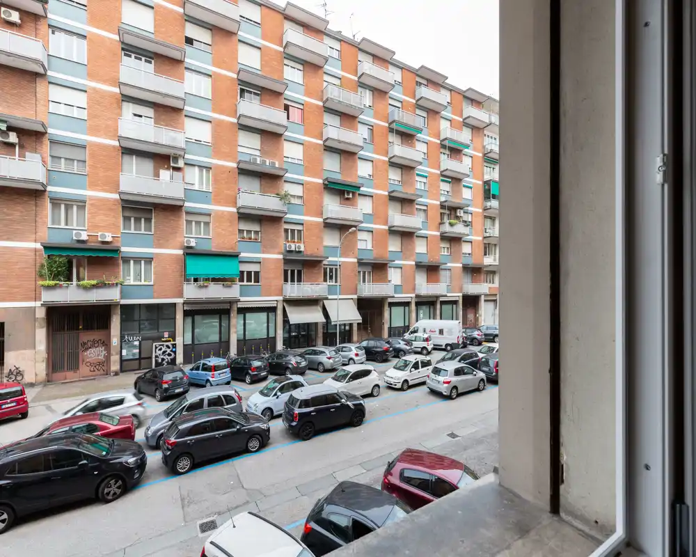 Street-facing view from a window showing parked cars and a residential building facade; useful for illustrating the neighbourhood and street context.