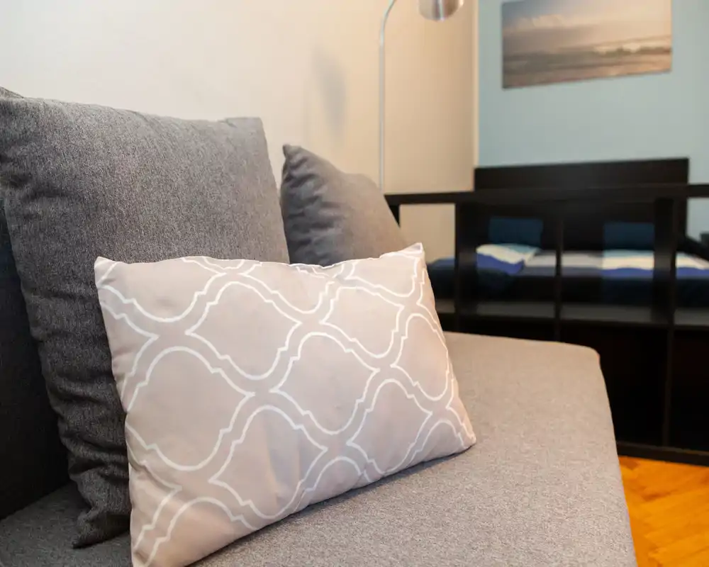 Bright, cozy living area focused on a gray sofa with patterned cushions and a modern floor lamp, suggesting a well-styled lounge space.