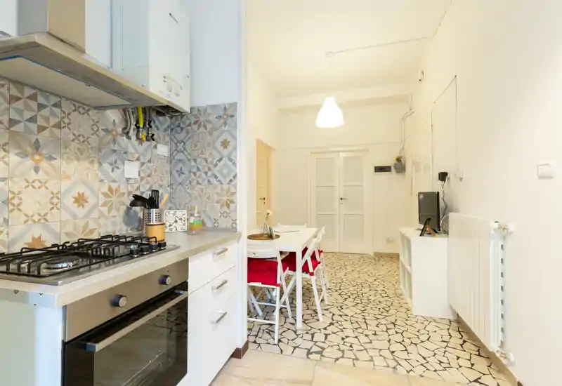 Angolo cottura luminoso e moderno con piastrelle decorative, piano cottura a gas e tavolo da pranzo adiacente — perfetto per un appartamento compatto.
