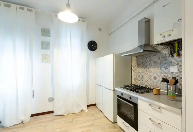 Cucina moderna e luminosa con piano cottura a gas, forno incassato e frigorifero a doppia anta. Piastrelle decorative sul paraschizzi e pavimento effetto legno offrono un'atmosfera calda e contemporanea.