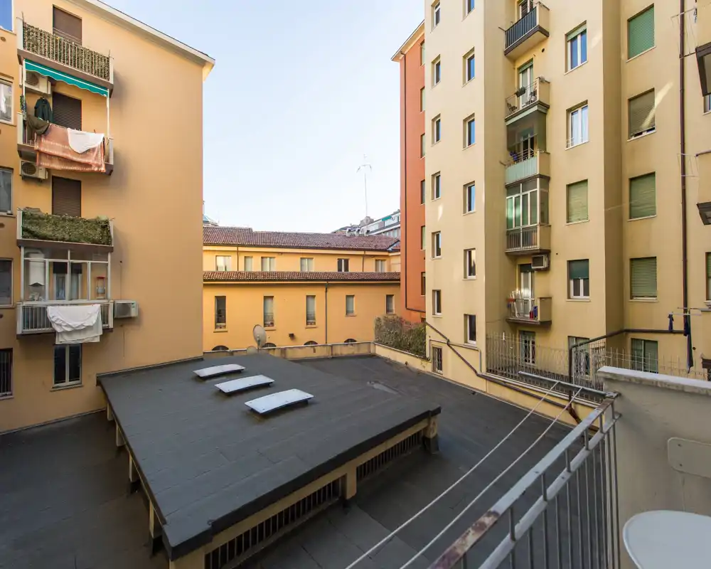 Vista desde un pequeño balcón al patio interior y los edificios contiguos. Se aprecian cubiertas, ventanas y balcones con luz natural.