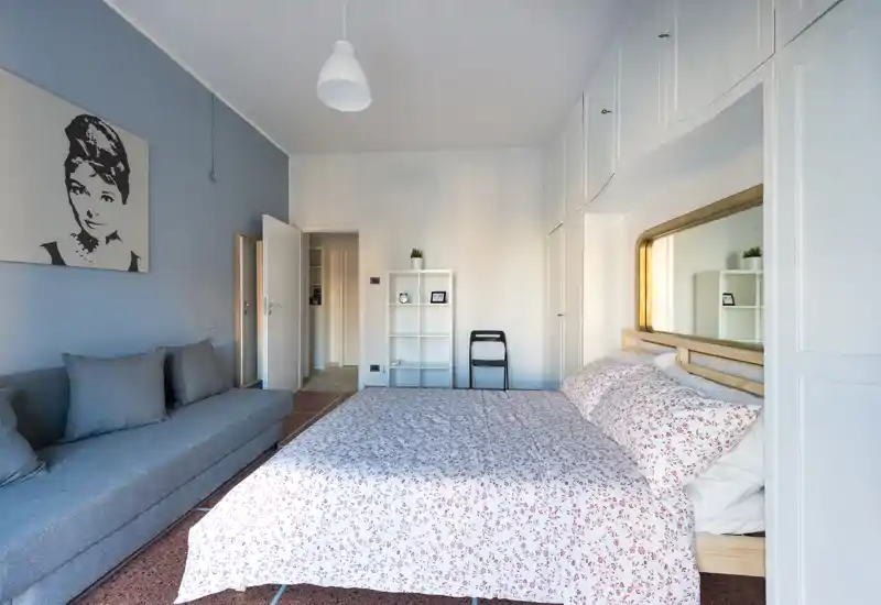 Dormitorio amplio y luminoso con cama doble grande vestida con ropa de cama floral, armarios empotrados alrededor de la cabecera y un sofá cómodo en la pared — espacio acogedor perfecto para descansar.