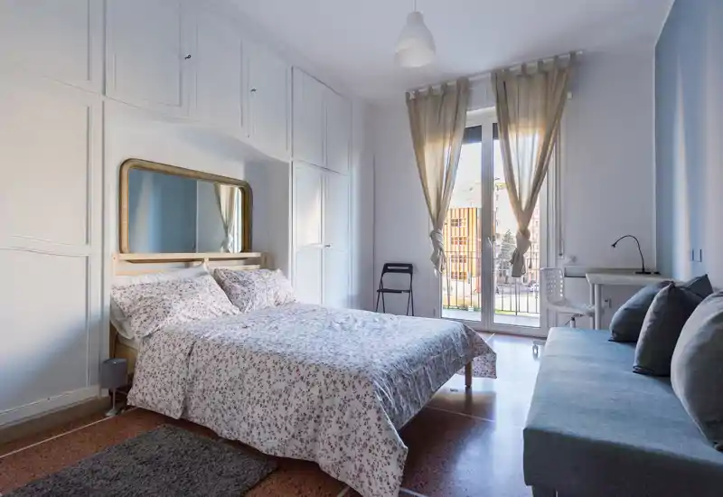 Dormitorio luminoso y bien acondicionado con cama doble, armarios empotrados y una pequeña zona de estar junto a la puerta-balcón que aporta mucha luz natural.