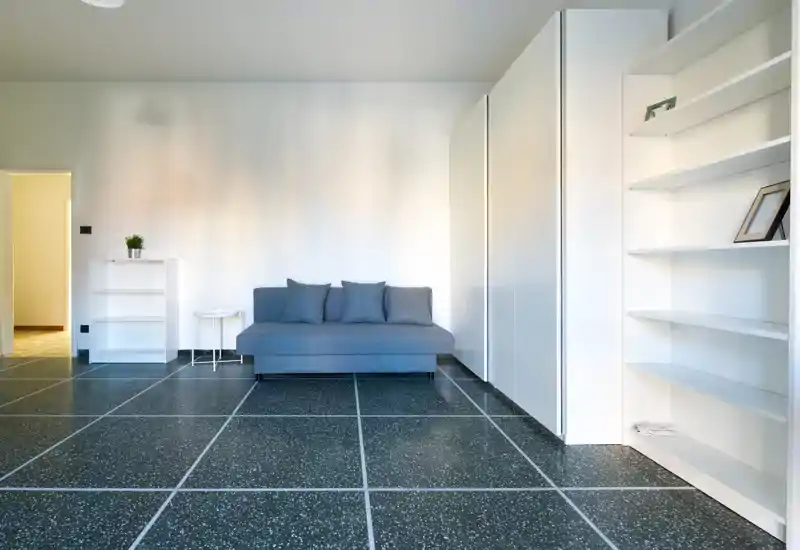 Minimal modern living room with a compact grey sofa, open shelving and bright, clean lines — a calm, well-lit lounge area ideal for a small apartment.