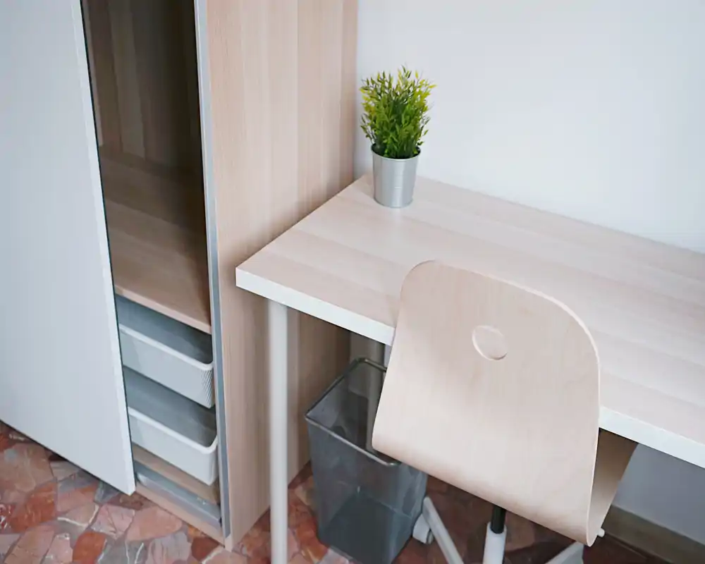 Rincón de escritorio luminoso y minimalista con mesa de madera clara, silla a juego y una pequeña planta en maceta—ideal como espacio de trabajo.