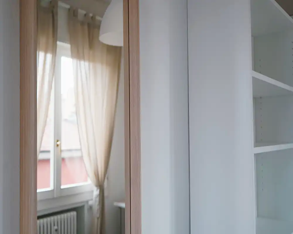 Rincón de dormitorio luminoso con cortinas translúcidas y estanterías empotradas; la foto destaca la luz de la ventana y una paleta neutra y relajante.