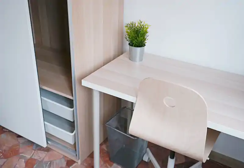 Rincón de escritorio luminoso y minimalista con mesa de madera clara, silla a juego y una pequeña planta en maceta—ideal como espacio de trabajo.