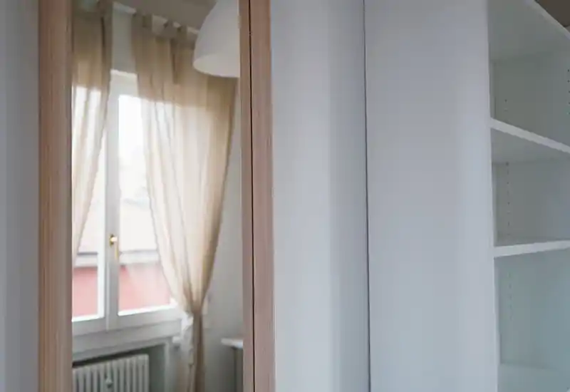 Rincón de dormitorio luminoso con cortinas translúcidas y estanterías empotradas; la foto destaca la luz de la ventana y una paleta neutra y relajante.