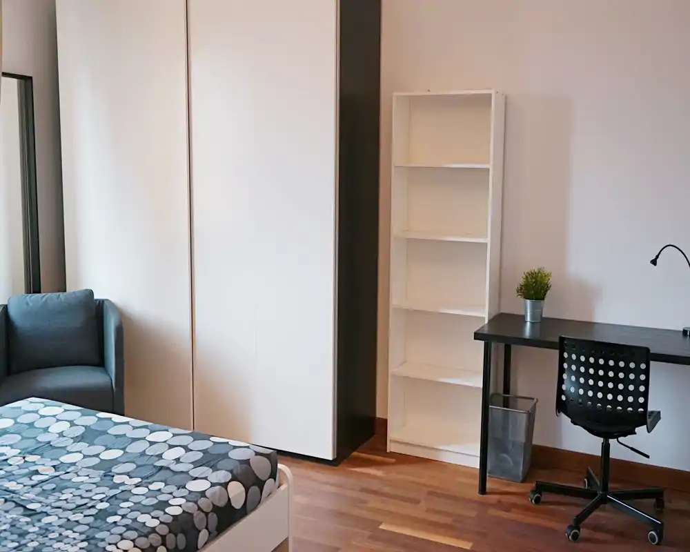 Dormitorio luminoso y minimalista con cama estampada, armario, estantería y pequeño escritorio — ordenado y funcional.