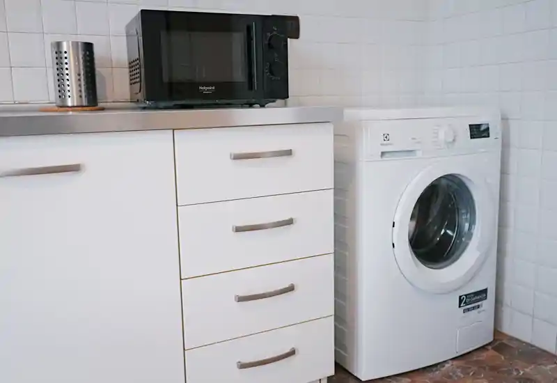 Compact kitchen corner with white cabinetry, countertop microwave and a front-loading washing machine — clean, functional layout ideal for small apartments.