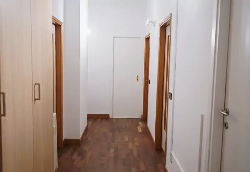 Bright, clean apartment corridor with wooden flooring, white walls and multiple doorways — ideal as an entrance or hallway view.