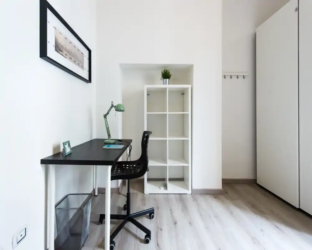 Minimal, bright bedroom corner with a study desk, shelving unit and wardrobe — clean Scandinavian-style space ideal for a single occupant or student.