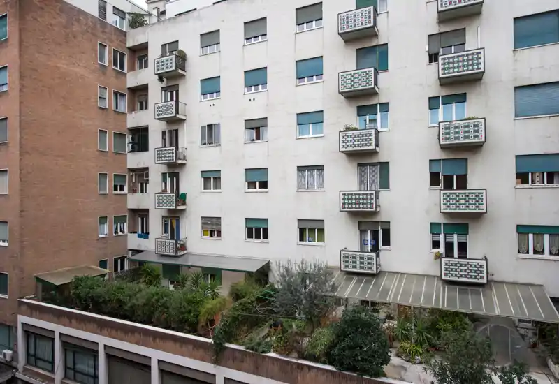 Vista del exterior de un edificio con varios balcones pequeños y una terraza ajardinada; adecuado para mostrar el espacio exterior y los balcones.