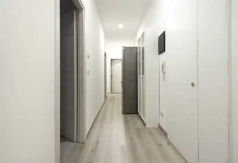 Ingresso/corridoio minimale e ben illuminato con pavimento in legno chiaro, pareti bianche e contenitori semplici. Spazio pulito e funzionale, adatto come corridoio d'ingresso dell'appartamento.