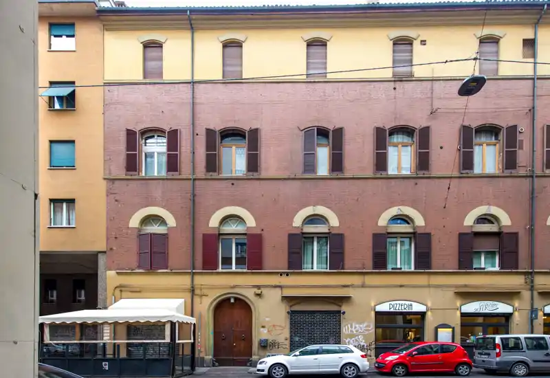 Facciata su strada con negozi a piano terra e auto parcheggiate; dettagli architettonici nitidi adatti a una vista esterna dell'immobile.