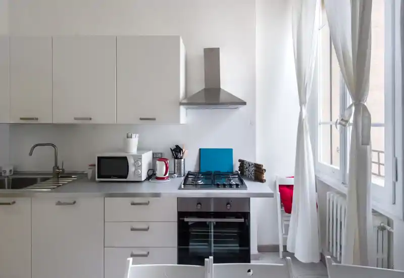 Cucina moderna e luminosa con mobili bianchi, piano cottura a gas, forno incassato e grande finestra che illumina l'ambiente: pulita e ben organizzata, perfetta per annunci.