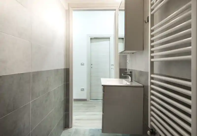 Bagno moderno e stretto con mobile lavabo sospeso, lavabo contemporaneo e termoarredo; piastrelle grigie neutre e stile minimal pulito.