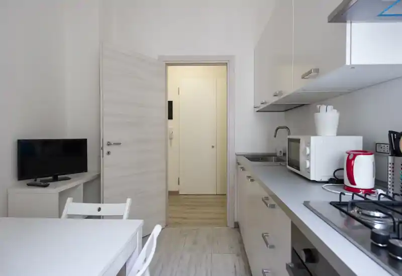 Cucina compatta e moderna con pensili bianchi, piano cottura a gas, microonde e bollitore, più un piccolo tavolo da pranzo — ben ordinata e adatta ad affitti brevi.
