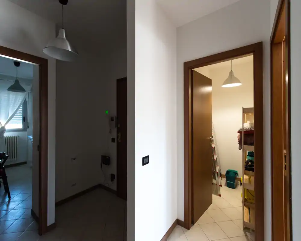 Ingresso con pavimento in piastrelle, pareti bianche e più porte che conducono ad altre stanze; ambiente pratico e ordinato con lampade a sospensione.
