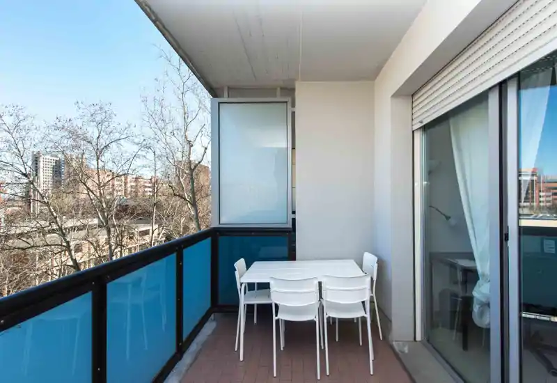 Bright balcony with a table and four chairs, glass railing and city views — ideal for outdoor dining or relaxing.