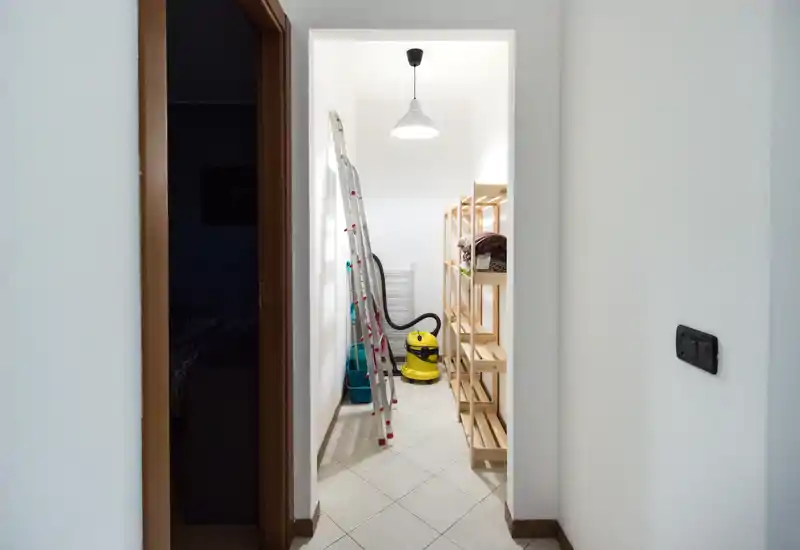 Small, well-lit storage alcove visible from the hallway with shelving, a ladder and cleaning equipment; suitable to advertise as a handy storage or utility space.