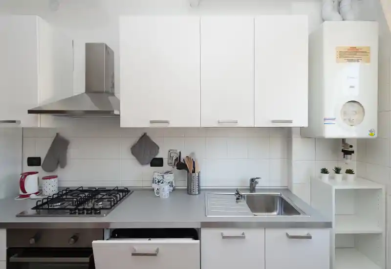 Bright, modern kitchen with gas hob, stainless sink and white cabinets. Neat countertop with small decorative items and practical utensils.