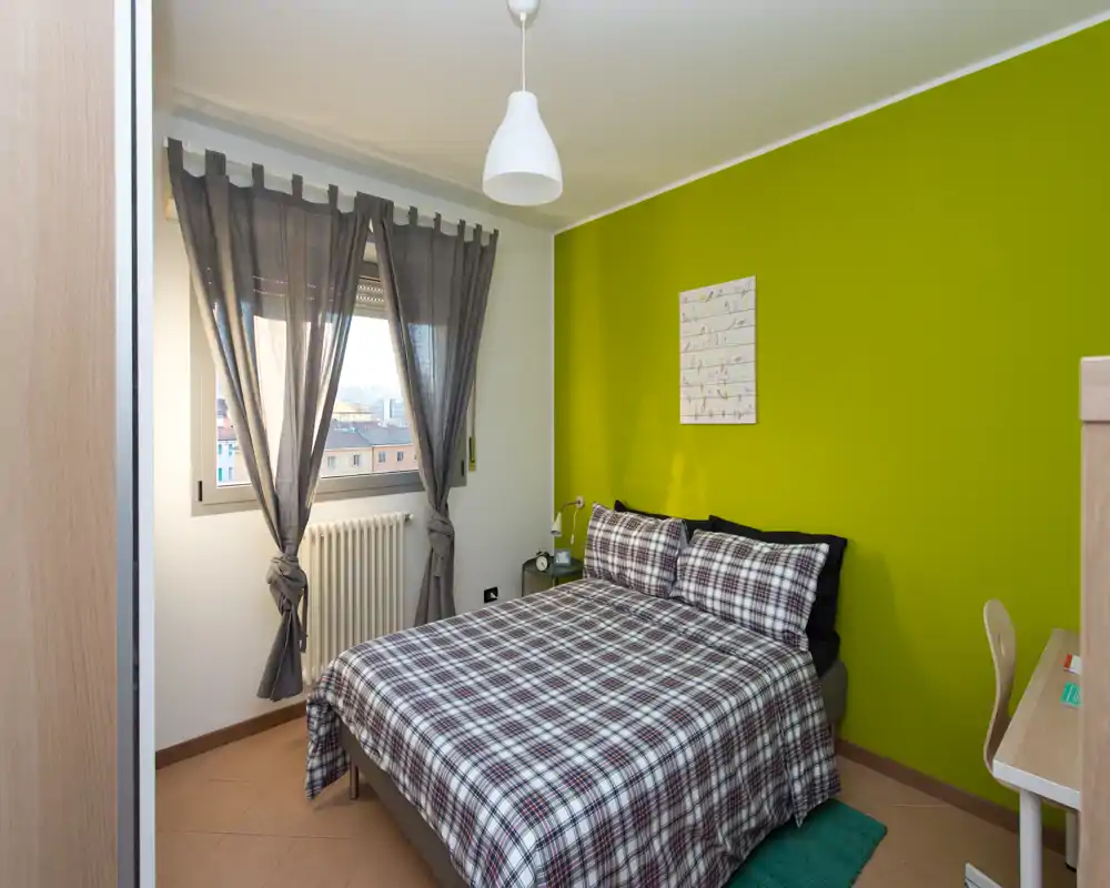 Dormitorio luminoso y bien compuesto con cama doble con ropa a cuadros, pared verde de acento y zona de escritorio — ideal para una estancia acogedora en la ciudad.