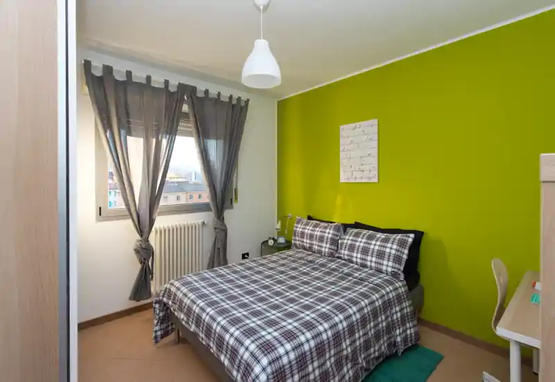 Dormitorio luminoso y bien compuesto con cama doble con ropa a cuadros, pared verde de acento y zona de escritorio — ideal para una estancia acogedora en la ciudad.