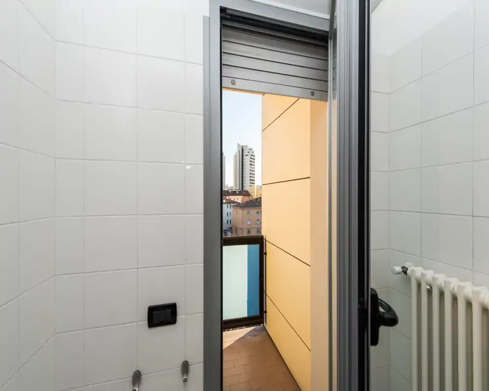 Pequeño balcón privado accesible desde una estancia con azulejos, con vistas a la ciudad y barandilla de vidrio de seguridad—ideal para un espacio exterior compacto.