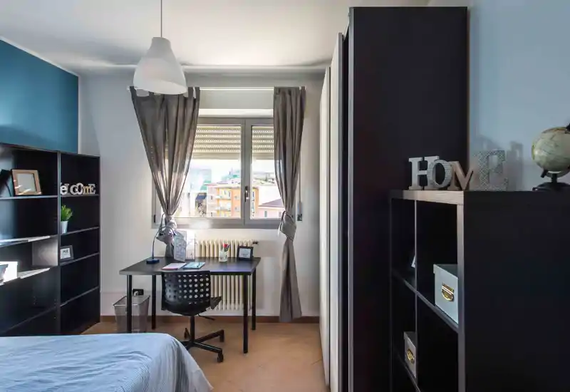 Dormitorio luminoso y ordenado con cama individual, escritorio junto a la ventana y estanterías organizadas. La luz natural lo hace ideal tanto para descansar como para trabajar.