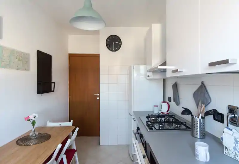 Bright, compact kitchen with a countertop gas hob, white cabinetry and a small wooden dining table with chairs — ideal for a cozy apartment.