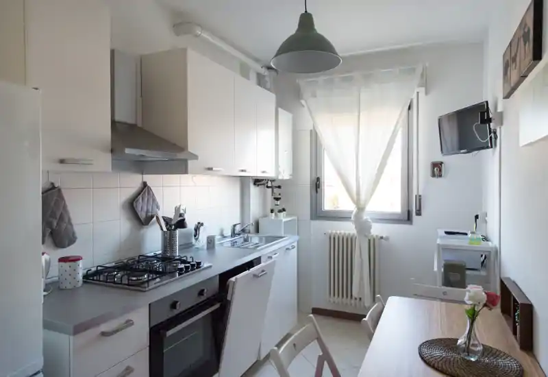 Bright, compact kitchen with white cabinetry, gas hob, built-in oven and a small dining table by the window — neat and well-styled for rental photos.